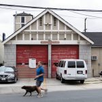 A man in a blue shirt runs past a dilapidated firehouse with his black dog.